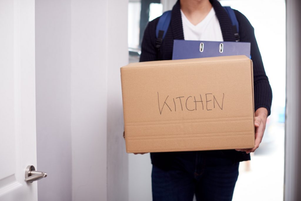 Close Up Of Male College Student Carrying Box Labeled Kitchen Moving Into Accommodation
