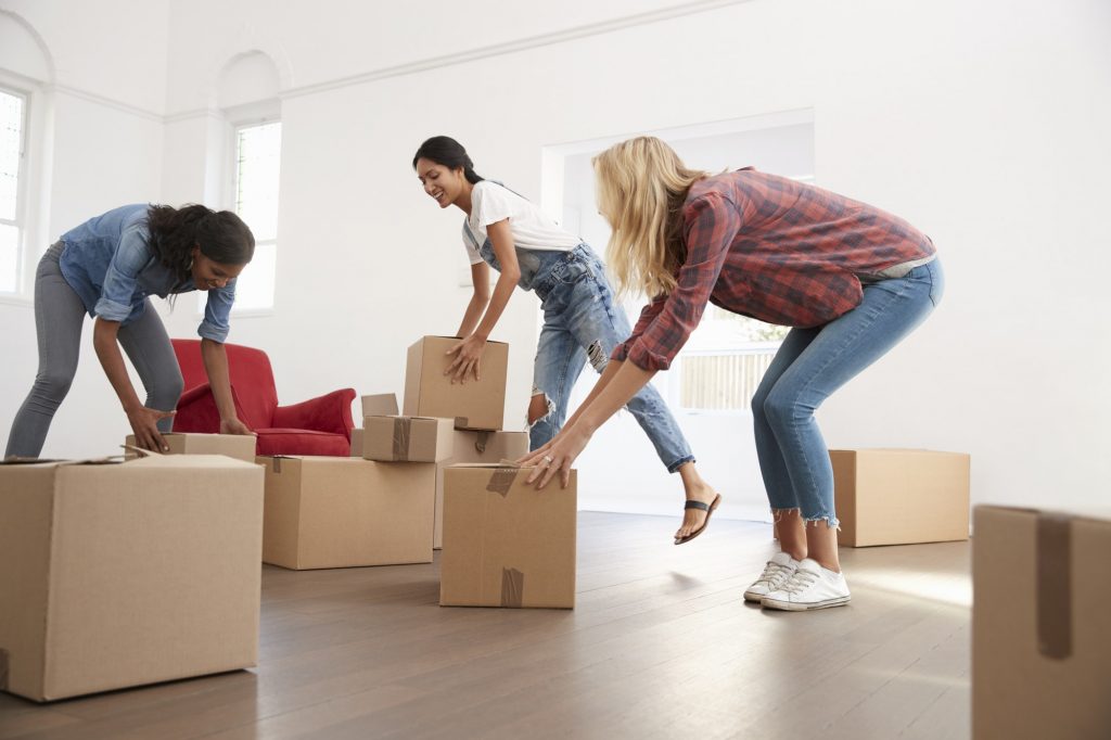 Three Female Friends Carrying Boxes Into New Home On Moving Day