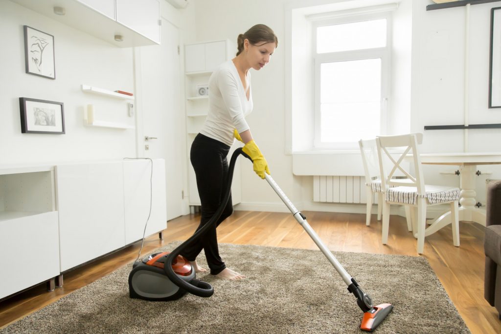 Woman in casual wear vacuum cleaning the carpet